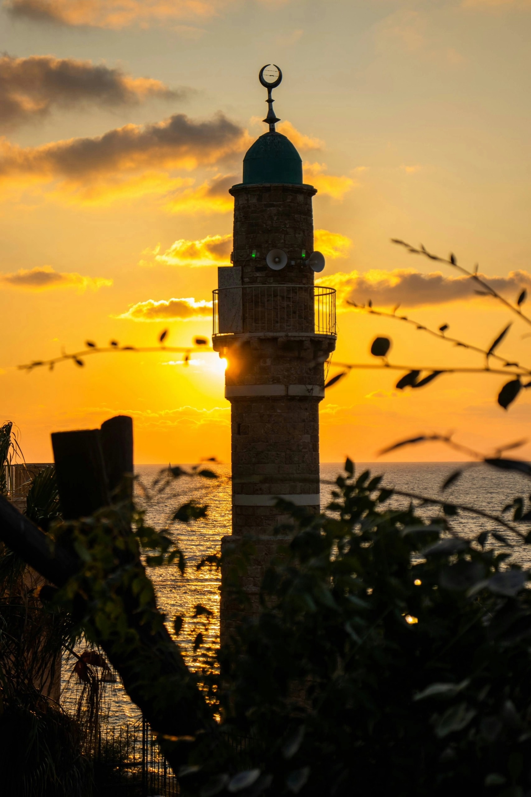 A minaret and mosque against a sunset sky beside the sea