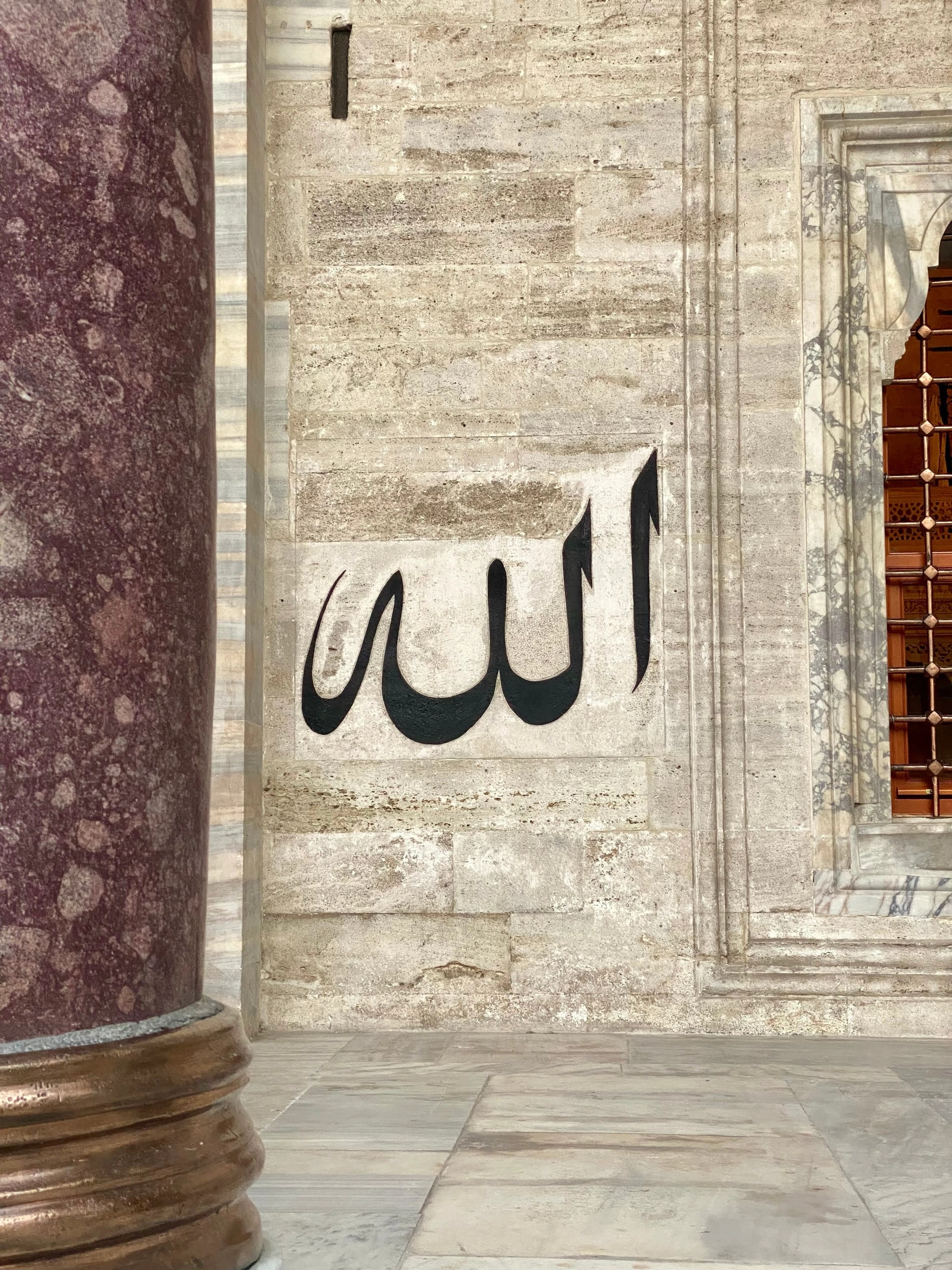 The name Allah in black calligraphy on a stone mosque wall