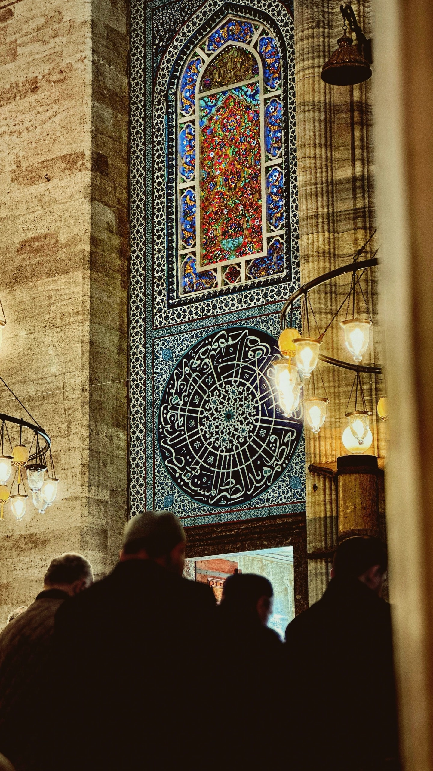 A tiled mihrab wall with a calligraphy roundel and hanging lamps