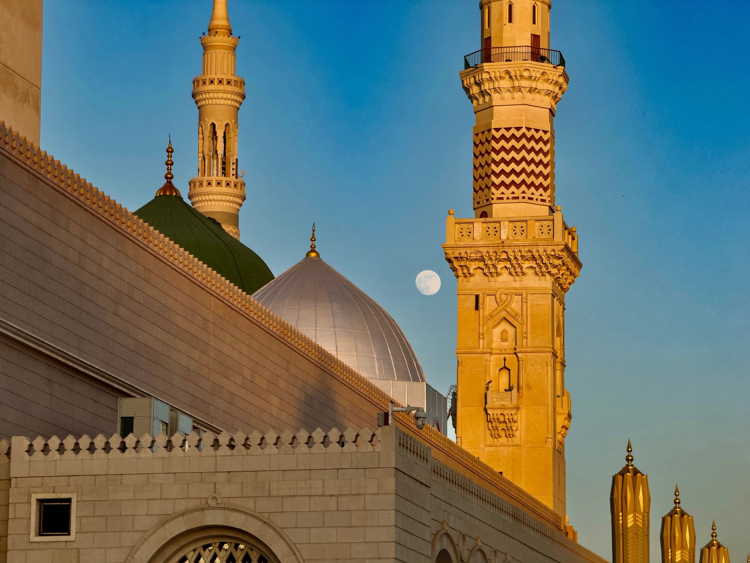A minaret and domes in Medina at golden hour, with the moon