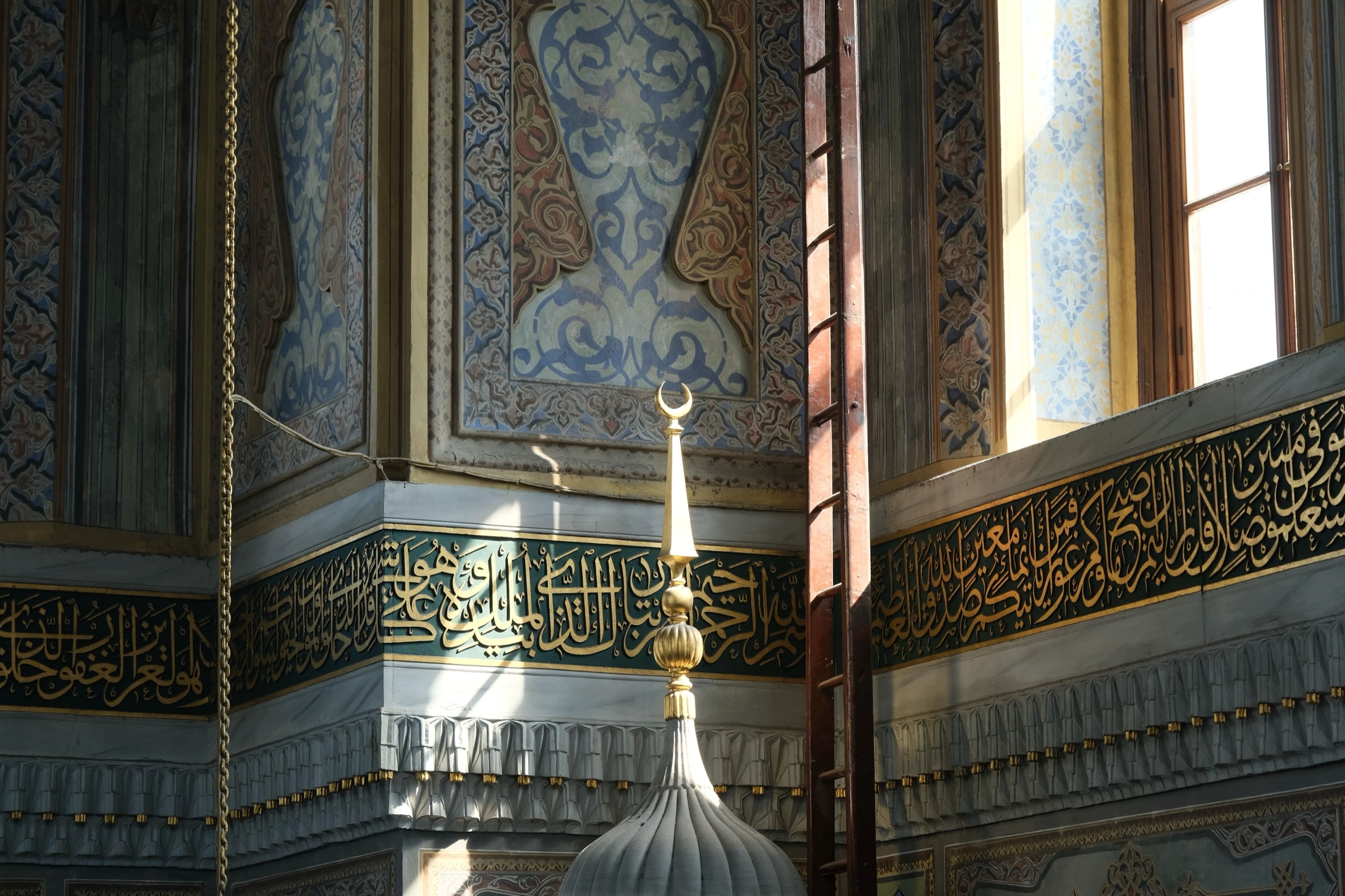 A band of gold calligraphy and a crescent finial inside a mosque